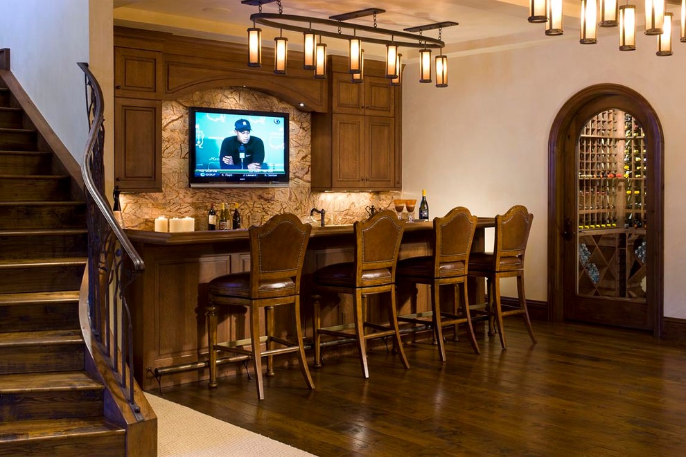This is an example of an expansive traditional single-wall seated home bar in Denver with an undermount sink, raised-panel cabinets, medium wood cabinets, copper benchtops, multi-coloured splashback, stone slab splashback and medium hardwood floors.