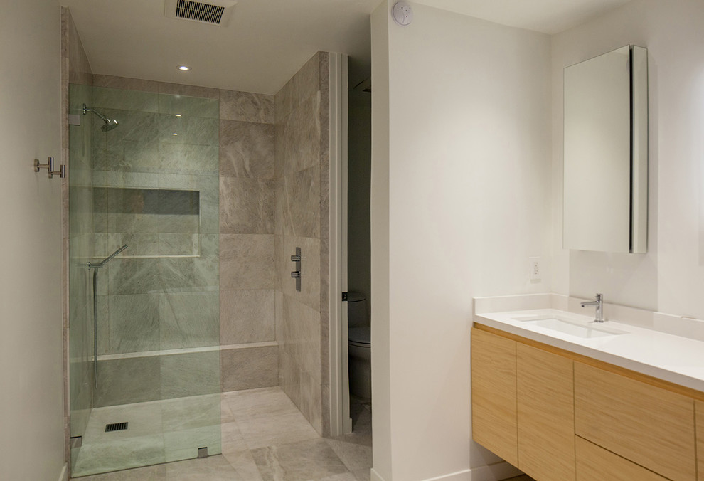 Inspiration for a mid-sized contemporary master bathroom in Los Angeles with flat-panel cabinets, light wood cabinets, a curbless shower, a two-piece toilet, gray tile, white tile, limestone, grey walls, limestone floors, an undermount sink, engineered quartz benchtops, grey floor, an open shower and white benchtops.