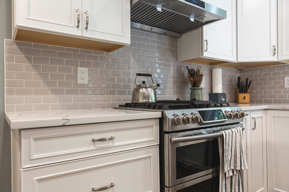 Large contemporary u-shaped open plan kitchen in DC Metro with an undermount sink, raised-panel cabinets, white cabinets, quartz benchtops, grey splashback, subway tile splashback, stainless steel appliances, vinyl floors, with island, brown floor and white benchtop.