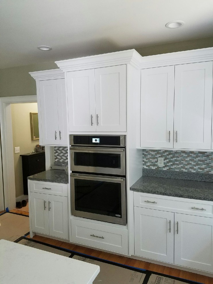 Large transitional light wood floor eat-in kitchen photo in Boston with recessed-panel cabinets, white cabinets, granite countertops, multicolored backsplash, glass tile backsplash and stainless steel appliances