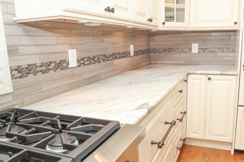 Large transitional u-shaped light wood floor eat-in kitchen photo in Newark with an undermount sink, raised-panel cabinets, distressed cabinets, granite countertops, brown backsplash, mosaic tile backsplash, stainless steel appliances and an island
