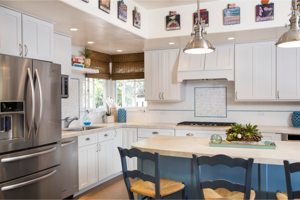 Inspiration for a mid-sized transitional l-shaped open plan kitchen in San Diego with a single-bowl sink, shaker cabinets, white cabinets, white splashback, subway tile splashback, stainless steel appliances, with island, quartz benchtops and porcelain floors.