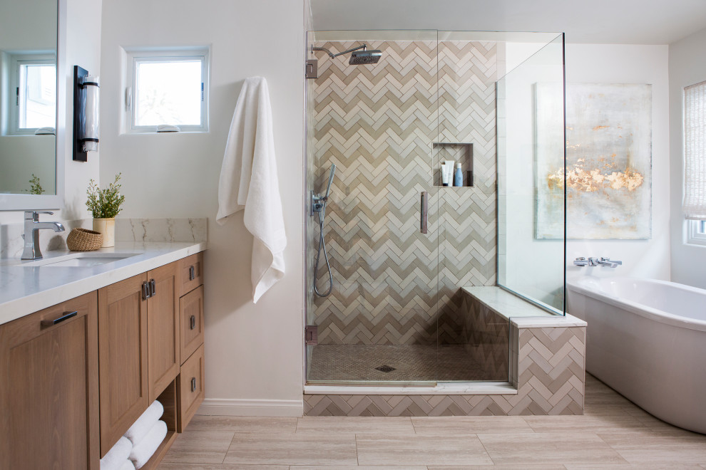 This is an example of a transitional master bathroom in Los Angeles with shaker cabinets, medium wood cabinets, a freestanding tub, an alcove shower, beige tile, gray tile, white tile, white walls, bamboo floors, an undermount sink, marble benchtops, brown floor, a hinged shower door, multi-coloured benchtops, a shower seat, a double vanity and a floating vanity.