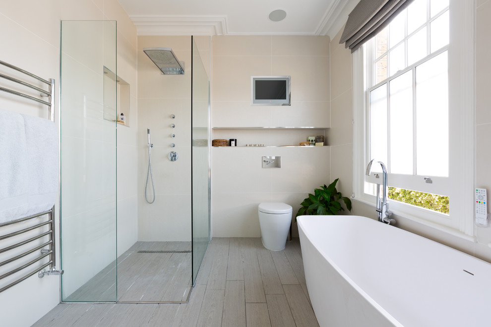 Contemporary master bathroom in London with a freestanding tub, a curbless shower, beige tile, light hardwood floors and a one-piece toilet.