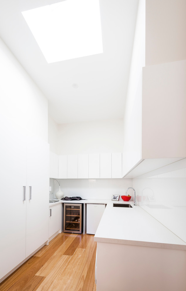 This is an example of a mid-sized contemporary u-shaped utility room in Melbourne with an undermount sink, white cabinets, white walls, medium hardwood floors and a side-by-side washer and dryer.