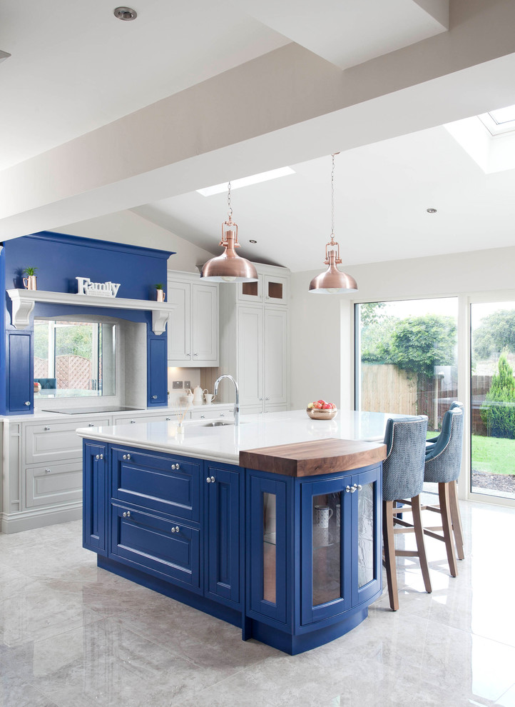 Expansive transitional l-shaped open plan kitchen in Dublin with an integrated sink, louvered cabinets, blue cabinets, quartzite benchtops, white splashback, stone slab splashback, stainless steel appliances, ceramic floors and with island.