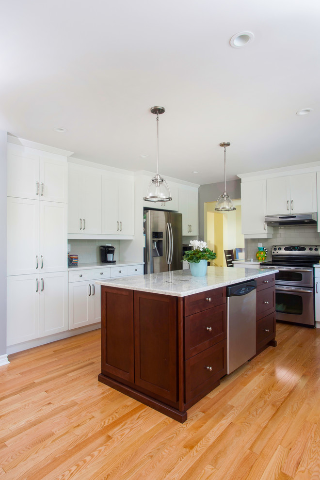 Large transitional u-shaped light wood floor eat-in kitchen photo with shaker cabinets, white cabinets, granite countertops, gray backsplash, glass tile backsplash, stainless steel appliances and an island