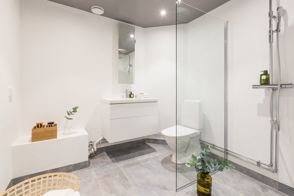 Mid-sized scandinavian master bathroom in Stockholm with flat-panel cabinets, white cabinets, an open shower, a two-piece toilet, white walls, limestone floors, a drop-in sink and an open shower.