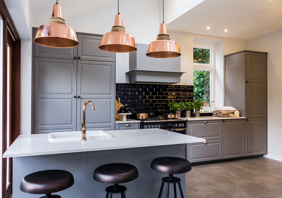 Inspiration for a large country open plan kitchen in London with raised-panel cabinets, grey cabinets, solid surface benchtops, ceramic splashback, porcelain floors, with island, black appliances and black splashback.