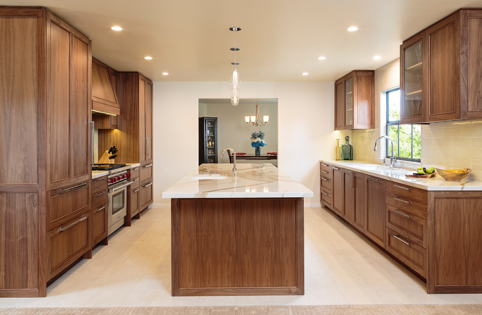 This is an example of a mid-sized transitional open plan kitchen in Los Angeles with an undermount sink, recessed-panel cabinets, medium wood cabinets, quartz benchtops, white splashback, ceramic splashback, stainless steel appliances, with island, beige floor, white benchtop and limestone floors.
