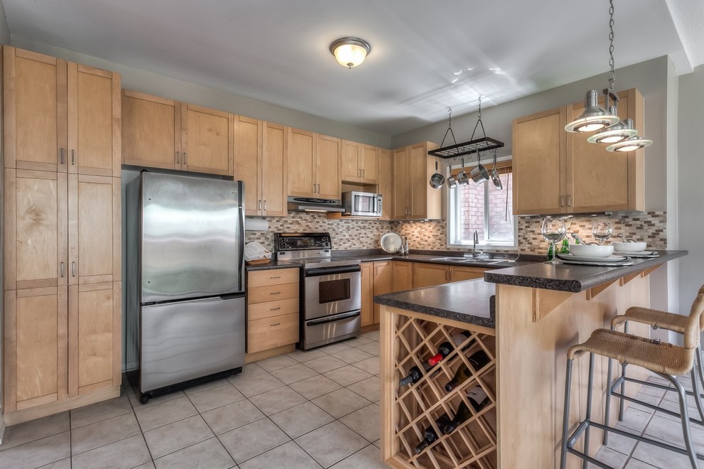 Mid-sized transitional u-shaped ceramic tile eat-in kitchen photo in Toronto with flat-panel cabinets, medium tone wood cabinets, laminate countertops, brown backsplash, glass tile backsplash, stainless steel appliances and an island