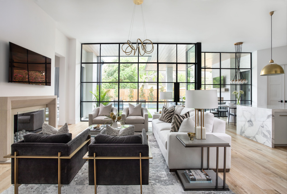 This is an example of an expansive transitional open concept living room in Houston with white walls, light hardwood floors, a standard fireplace, a wall-mounted tv and brown floor.