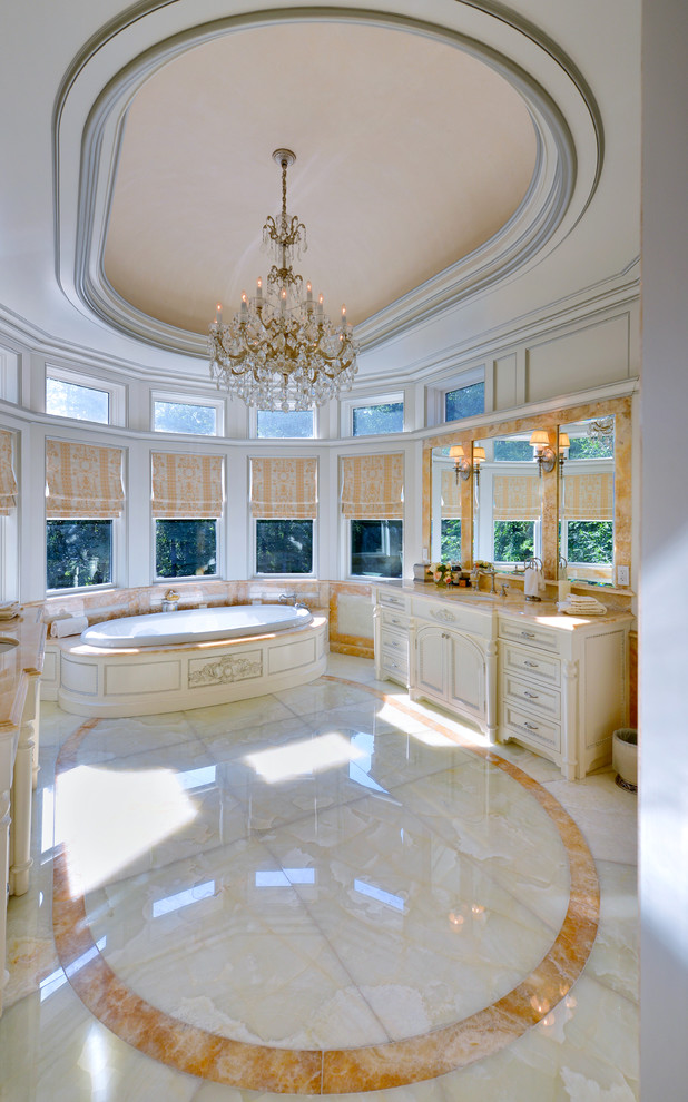 This is an example of an expansive traditional master bathroom in New York with an undermount sink, furniture-like cabinets, light wood cabinets, onyx benchtops, a drop-in tub, a one-piece toilet, beige tile, stone slab, beige walls and marble floors.