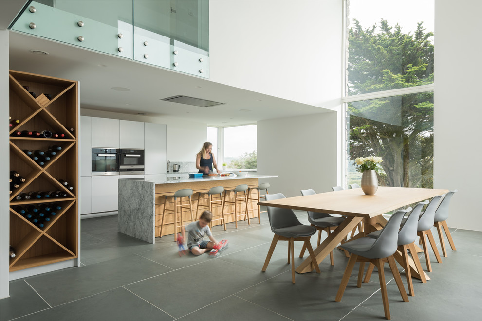 This is an example of a large contemporary eat-in kitchen in Cornwall with flat-panel cabinets, white cabinets, marble benchtops, slate floors, grey floor and with island.