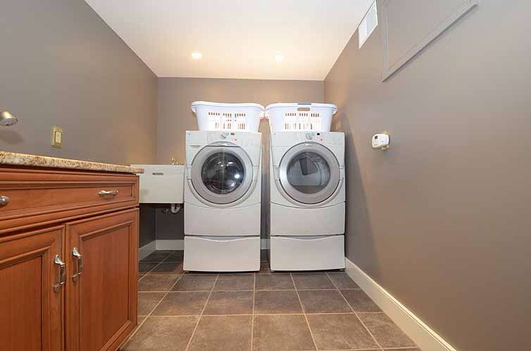 This is an example of a mid-sized traditional single-wall dedicated laundry room in Philadelphia with an utility sink, beaded inset cabinets, medium wood cabinets, granite benchtops, beige walls, ceramic floors and a side-by-side washer and dryer.