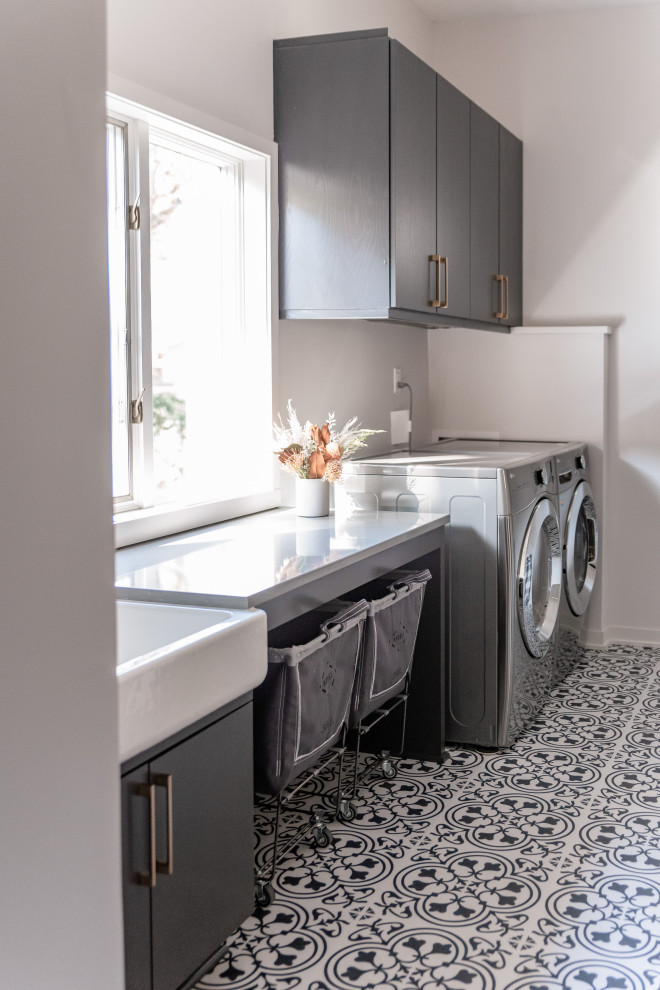 Inspiration for a transitional laundry room in Omaha with a farmhouse sink, white walls, a side-by-side washer and dryer and grey benchtop.