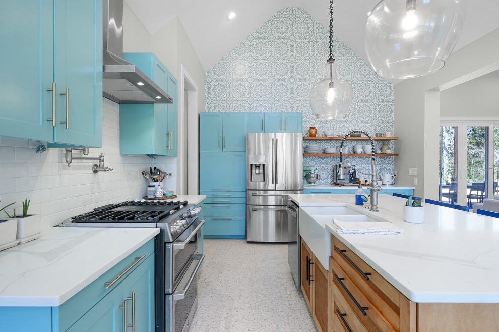 Design ideas for a large country l-shaped open plan kitchen in Dallas with a farmhouse sink, flat-panel cabinets, blue cabinets, quartz benchtops, white splashback, ceramic splashback, stainless steel appliances, terrazzo floors, with island, white floor, white benchtop and vaulted.