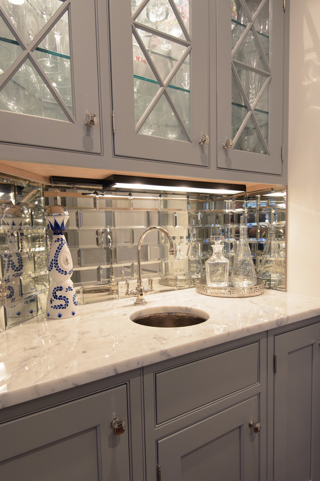 This is an example of a small transitional single-wall wet bar in New York with an undermount sink, glass-front cabinets, grey cabinets, marble benchtops, subway tile splashback and dark hardwood floors.