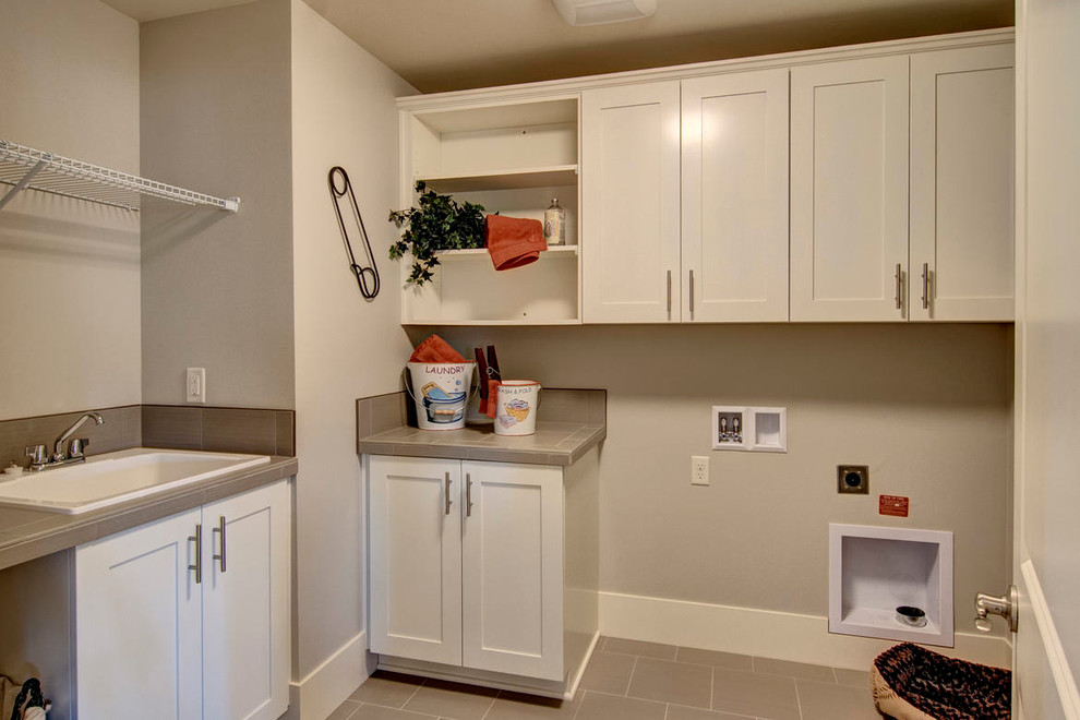 Transitional l-shaped dedicated laundry room in Seattle with a drop-in sink, flat-panel cabinets, white cabinets, solid surface benchtops, beige walls, ceramic floors and a side-by-side washer and dryer.