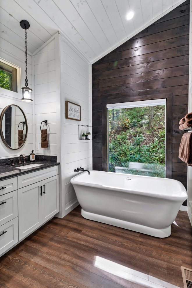 Inspiration for a medium sized modern ensuite bathroom in Houston with recessed-panel cabinets, white cabinets, an alcove bath, white walls, dark hardwood flooring, a submerged sink, brown floors, black worktops, double sinks, a built in vanity unit, a vaulted ceiling and tongue and groove walls.