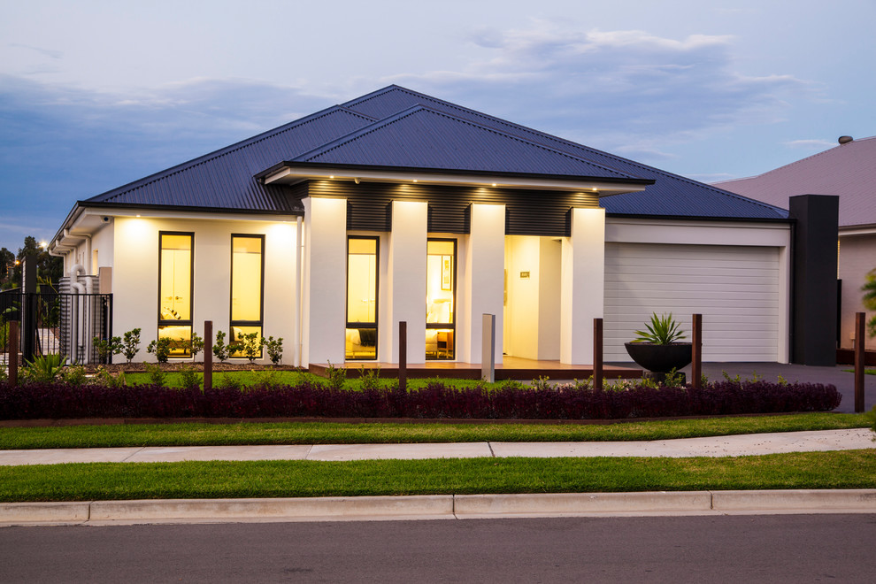 This is an example of a large contemporary one-storey stucco beige house exterior in Newcastle - Maitland with a metal roof.