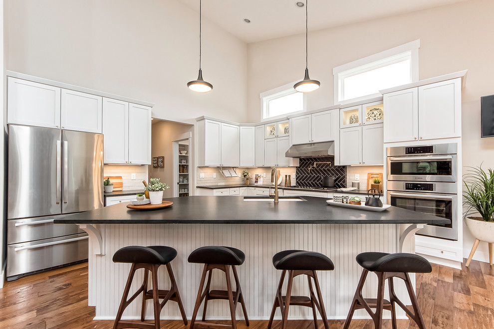 Mid-sized transitional u-shaped kitchen in Columbus with an undermount sink, shaker cabinets, white cabinets, black splashback, stainless steel appliances, medium hardwood floors, with island and brown floor.
