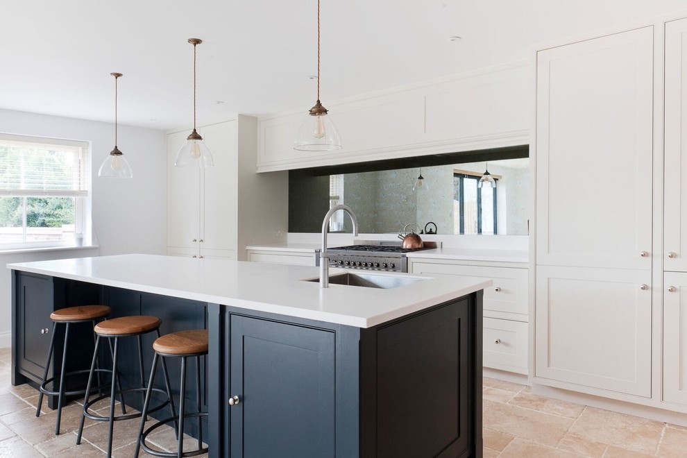 Mid-sized transitional kitchen in Essex with mirror splashback, stainless steel appliances, with island, white benchtop, a single-bowl sink, beaded inset cabinets, beige floor, travertine floors and white cabinets.