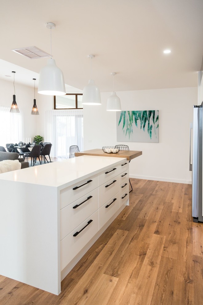 Contemporary galley open plan kitchen in Other with a double-bowl sink, flat-panel cabinets, white cabinets, granite benchtops, white splashback, porcelain splashback, stainless steel appliances, laminate floors, with island and brown floor.