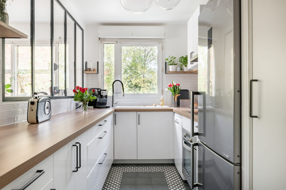 Design ideas for a mid-sized scandinavian u-shaped kitchen in Paris with an undermount sink, white cabinets, laminate benchtops, white splashback, subway tile splashback, black appliances, cement tiles, no island, grey floor and brown benchtop.