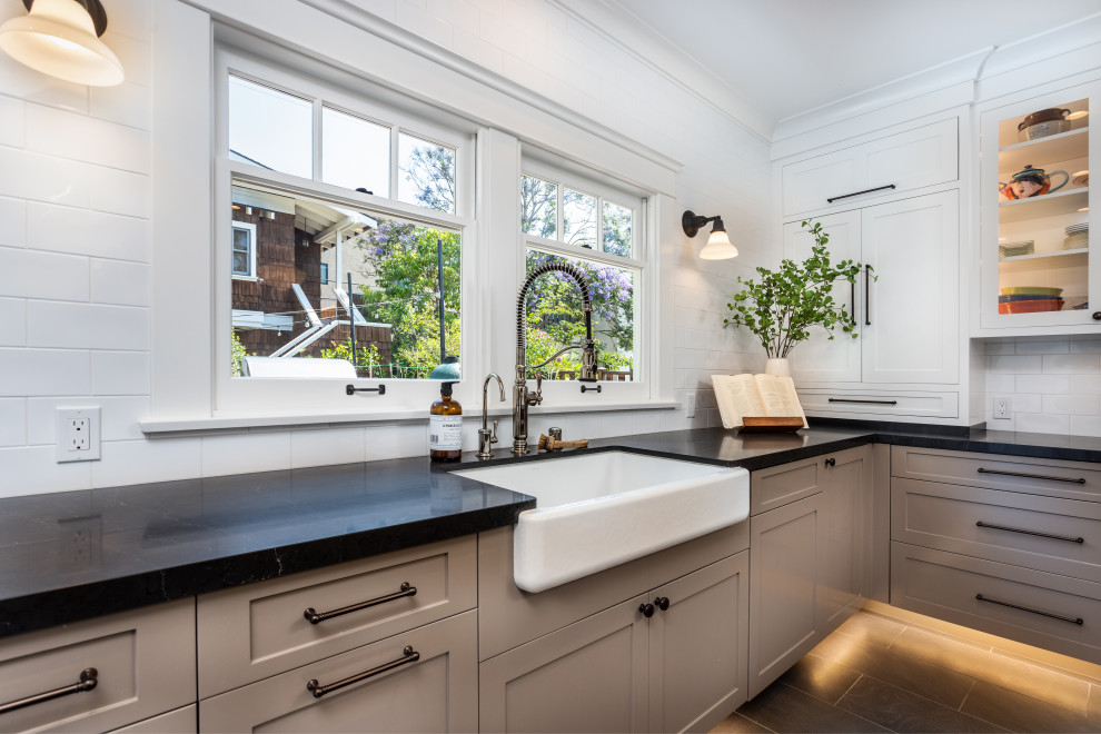 Design ideas for a mid-sized arts and crafts separate kitchen in Los Angeles with a farmhouse sink, beige cabinets, white splashback, subway tile splashback, panelled appliances, with island, grey floor and black benchtop.
