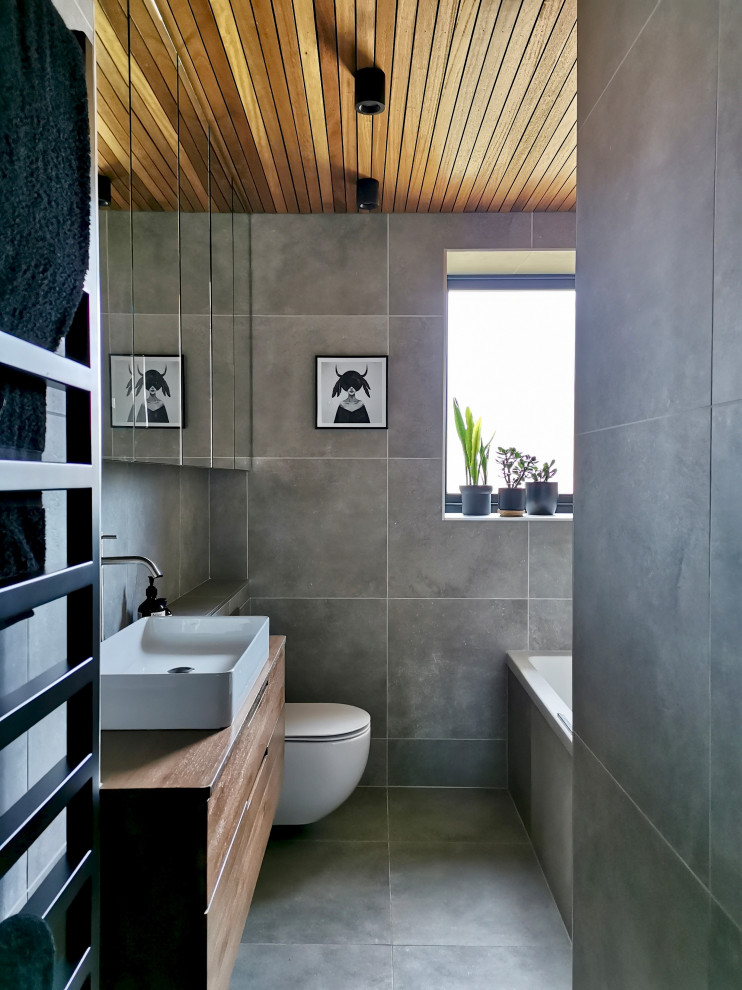 Inspiration for a small contemporary bathroom in Other with flat-panel cabinets, brown cabinets, a drop-in tub, a shower/bathtub combo, a wall-mount toilet, gray tile, porcelain tile, grey walls, porcelain floors, grey floor, a single vanity, a floating vanity and timber.