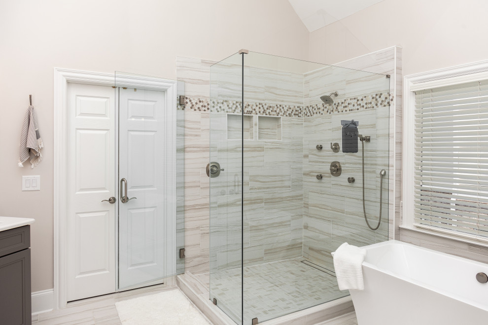Photo of an expansive contemporary master bathroom in Atlanta with recessed-panel cabinets, grey cabinets, a freestanding tub, a two-piece toilet, porcelain tile, beige walls, porcelain floors, an undermount sink, engineered quartz benchtops, a hinged shower door, white benchtops, a niche, a double vanity, a built-in vanity and vaulted.
