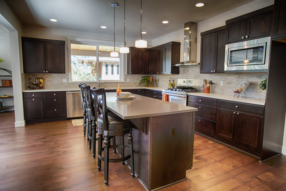 Photo of a large traditional u-shaped open plan kitchen in Seattle with an undermount sink, flat-panel cabinets, dark wood cabinets, quartzite benchtops, beige splashback, stone tile splashback, stainless steel appliances, medium hardwood floors, with island and brown floor.
