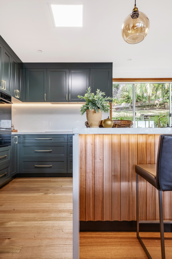 Inspiration for a large transitional l-shaped medium tone wood floor and multicolored floor eat-in kitchen remodel in Sydney with a drop-in sink, shaker cabinets, green cabinets, quartz countertops, white backsplash, quartz backsplash, black appliances, an island and white countertops