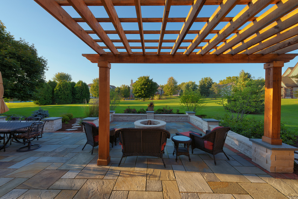 This is an example of a large traditional backyard patio in Milwaukee with a fire feature, tile and a pergola.
