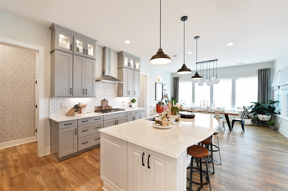 This is an example of an industrial kitchen in Charlotte with grey cabinets, quartz benchtops, white splashback, subway tile splashback, stainless steel appliances, light hardwood floors, with island, beige floor and white benchtop.