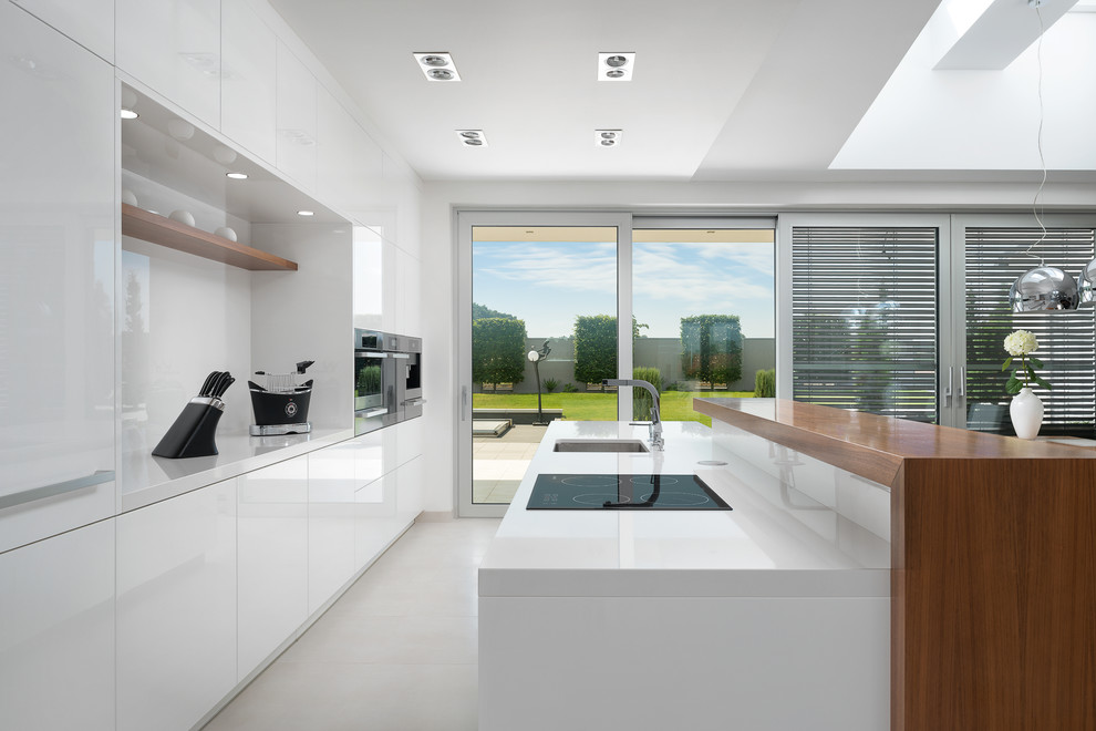 This is an example of a mid-sized modern galley open plan kitchen in Other with an undermount sink, flat-panel cabinets, white cabinets, white splashback, glass sheet splashback, stainless steel appliances, ceramic floors and with island.