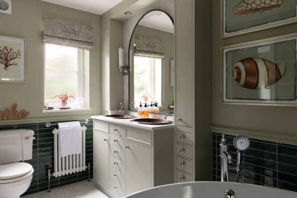 Inspiration for a medium sized farmhouse ensuite half tiled bathroom in Surrey with flat-panel cabinets, green cabinets, a freestanding bath, a one-piece toilet, green tiles, porcelain tiles, green walls, porcelain flooring, a built-in sink, quartz worktops, white floors, white worktops, double sinks and a built in vanity unit.