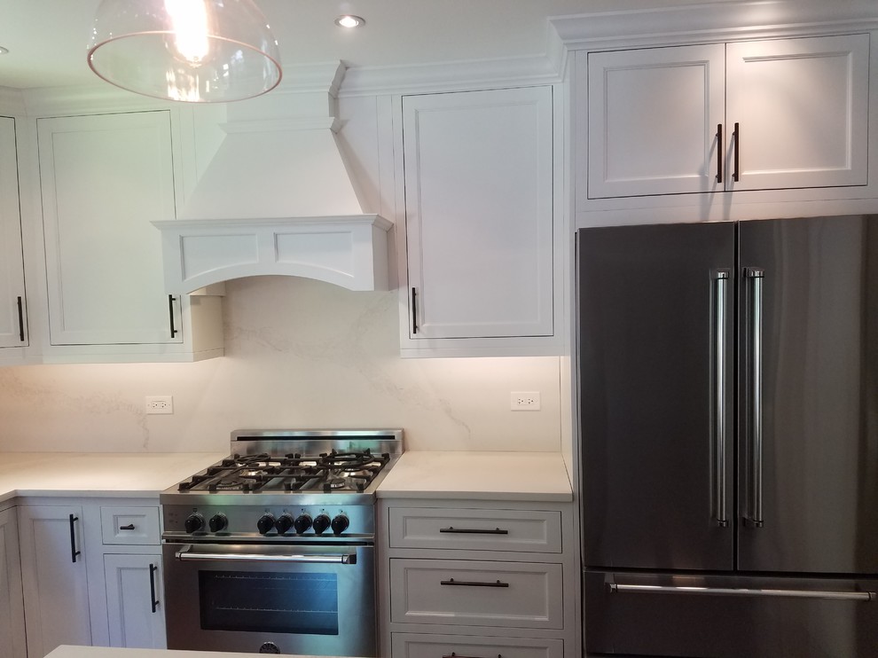 Eat-in kitchen - mid-sized transitional l-shaped medium tone wood floor and brown floor eat-in kitchen idea in Chicago with a farmhouse sink, recessed-panel cabinets, white cabinets, quartz countertops, white backsplash, stainless steel appliances and an island