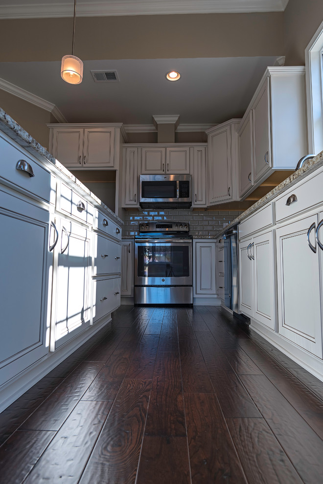 Example of a mid-sized transitional l-shaped dark wood floor open concept kitchen design with an undermount sink, recessed-panel cabinets, white cabinets, granite countertops, gray backsplash, subway tile backsplash, stainless steel appliances and an island