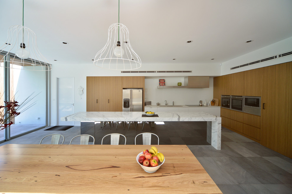 Photo of a large contemporary l-shaped eat-in kitchen in Melbourne with a drop-in sink, flat-panel cabinets, medium wood cabinets, marble benchtops, white splashback, glass sheet splashback and with island.