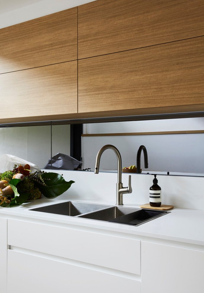 Large contemporary l-shaped kitchen pantry in Sydney with a double-bowl sink, flat-panel cabinets, white cabinets, quartz benchtops, multi-coloured splashback, mirror splashback, black appliances, laminate floors, with island and multi-coloured benchtop.