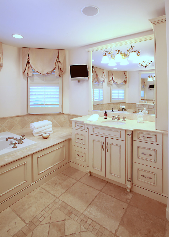 Photo of a mid-sized traditional master bathroom in Providence with an undermount sink, beige tile, beige walls, recessed-panel cabinets, distressed cabinets, limestone benchtops, a drop-in tub, stone tile and limestone floors.