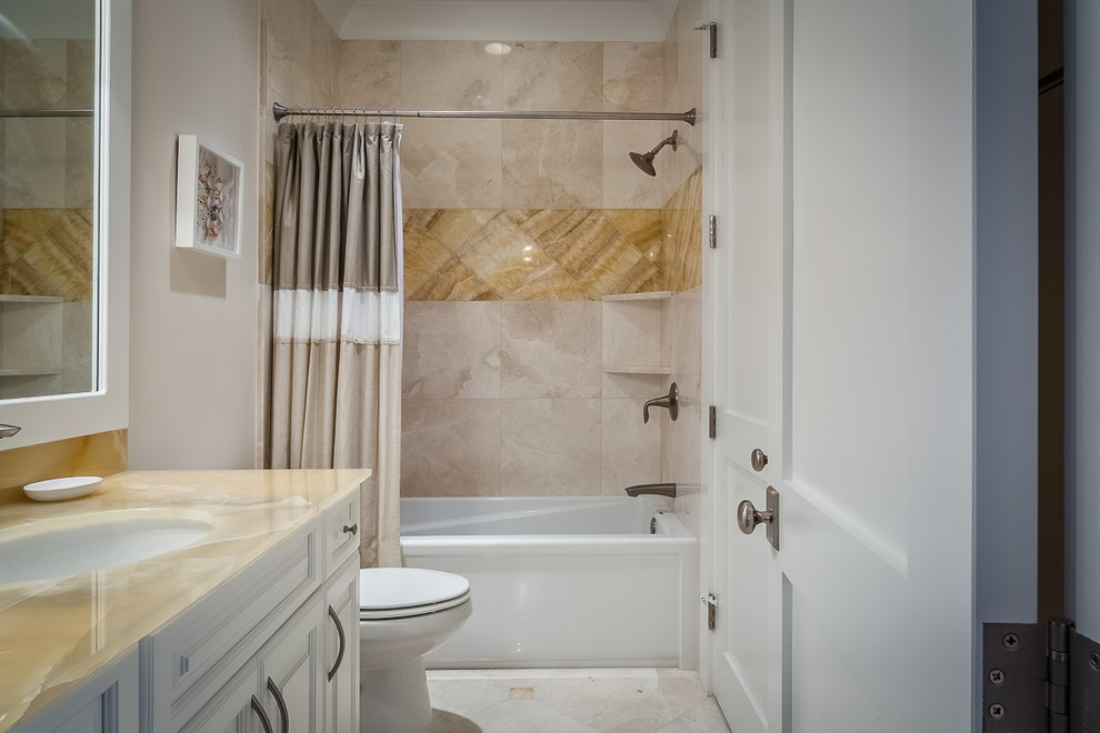 Inspiration for a mid-sized transitional kids bathroom in Charleston with an undermount sink, recessed-panel cabinets, white cabinets, an alcove tub, a shower/bathtub combo, a one-piece toilet, beige walls, marble floors and glass benchtops.