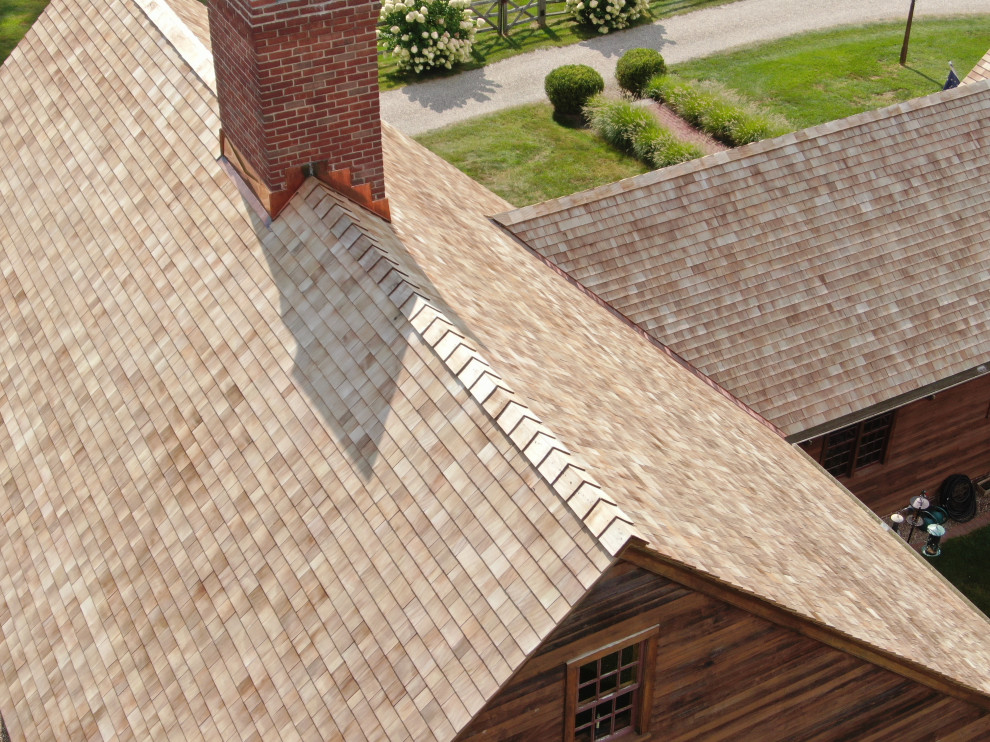 Esempio della villa grande marrone country a tre piani con rivestimento in legno, tetto a capanna, copertura a scandole, tetto rosso e pannelli sovrapposti