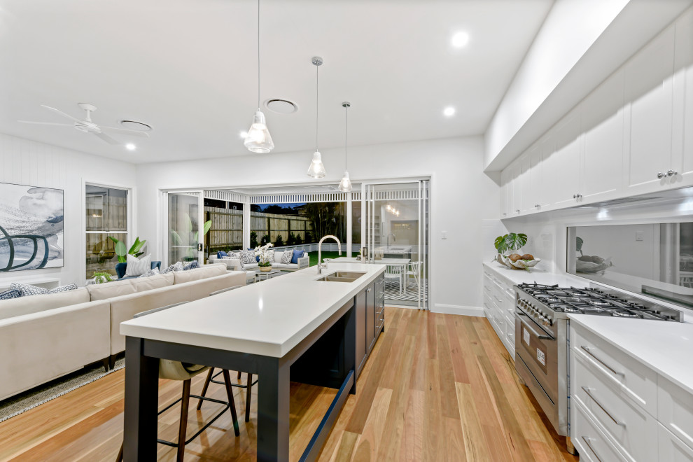 Photo of a large galley kitchen pantry in Brisbane with an undermount sink, shaker cabinets, white cabinets, quartz benchtops, white splashback, subway tile splashback, stainless steel appliances, light hardwood floors, with island, brown floor and white benchtop.