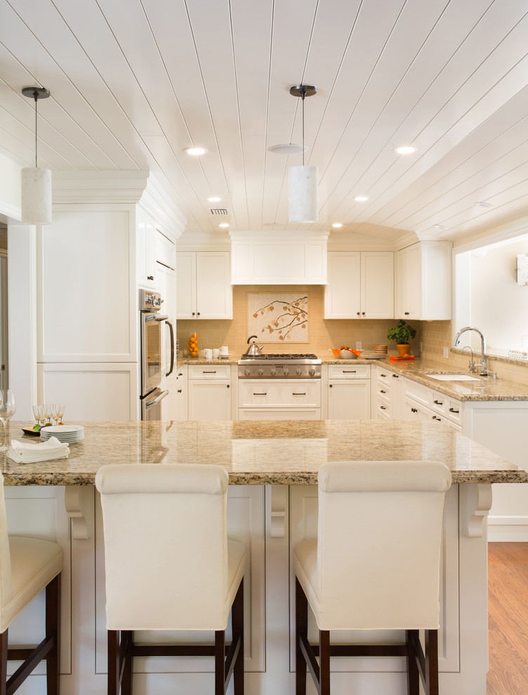 This is an example of a mid-sized traditional u-shaped open plan kitchen in Los Angeles with an undermount sink, shaker cabinets, white cabinets, granite benchtops, yellow splashback, subway tile splashback, stainless steel appliances, medium hardwood floors and a peninsula.