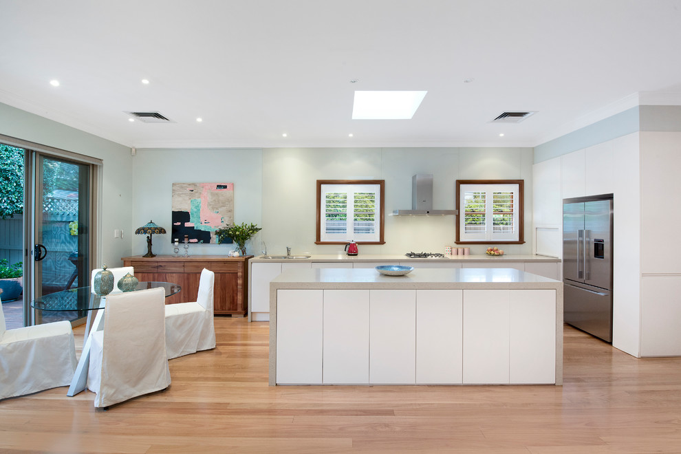 Inspiration for a transitional l-shaped eat-in kitchen in Sydney with an undermount sink, flat-panel cabinets, white cabinets, solid surface benchtops, green splashback, glass sheet splashback, stainless steel appliances, light hardwood floors, with island and beige benchtop.