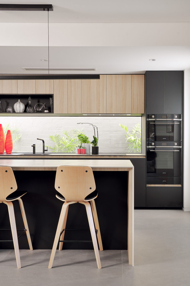 Cette image montre une cuisine ouverte design en bois clair avec un placard à porte plane, plan de travail carrelé, fenêtre, un électroménager noir, un sol en carrelage de porcelaine, îlot et un sol gris.