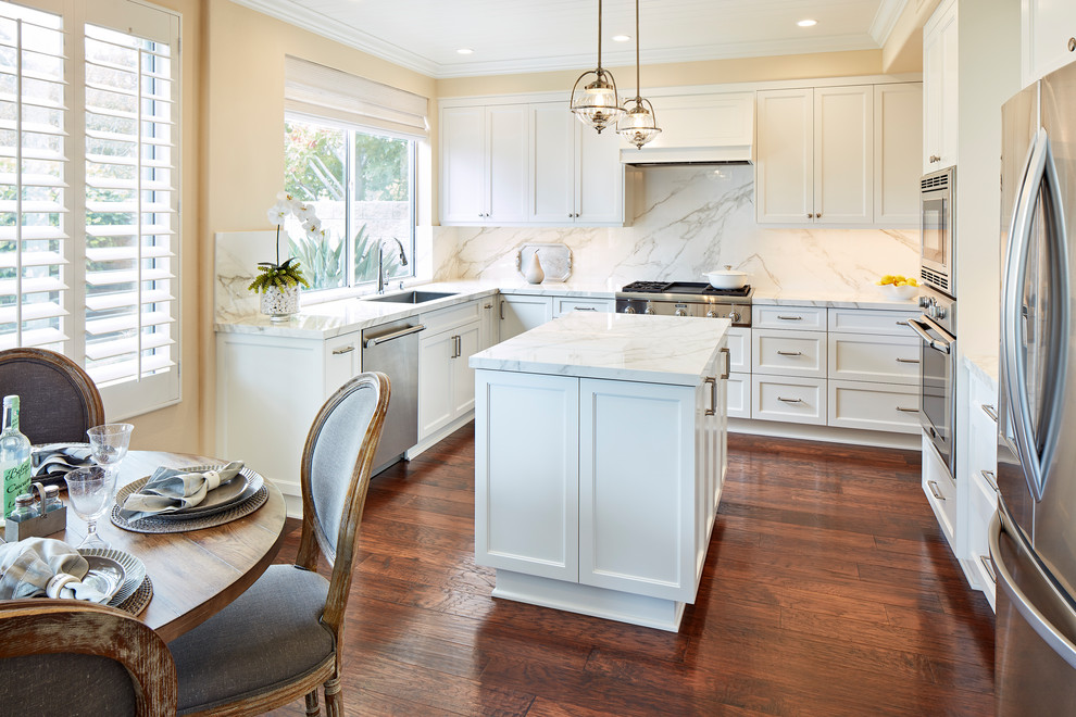 Inspiration for a large transitional l-shaped eat-in kitchen in Orange County with with island, an undermount sink, white cabinets, white splashback, stainless steel appliances, dark hardwood floors, brown floor, white benchtop, recessed-panel cabinets and quartz benchtops.